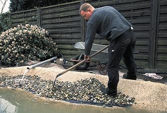 Teichbau Schritt 9: Der Ranbereich wird mit Kieselsteinen gefüllt und mir einer Schaufel verteilt.