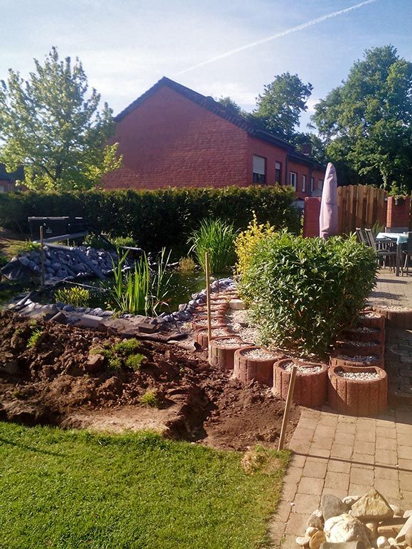 Der Koiteich passt sich perfekt an die Terrasse an, das Blumenbeet neben dem Teich ist noch unbepflanzt.